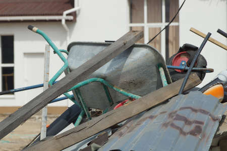 one old gray metal broken garden wheelbarrow lies on a pile of rubbish among wooden planks on the streetの写真素材