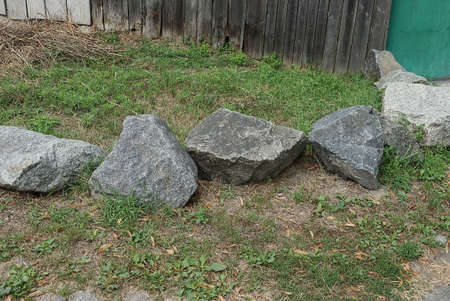 a row of big gray stones lie on the green grass on the streetの写真素材