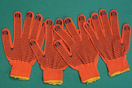 four red work gloves made of fabric lies on a green table
