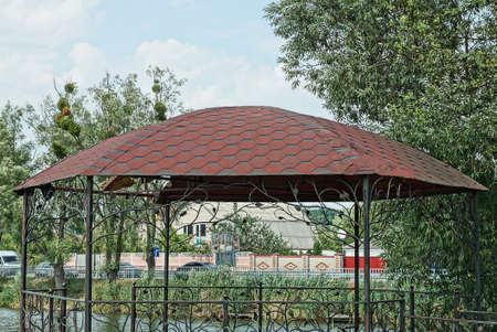 part of an empty black metal gazebo under an extreme korotichnevy tiled roof against a background of blue sky and green treesの写真素材