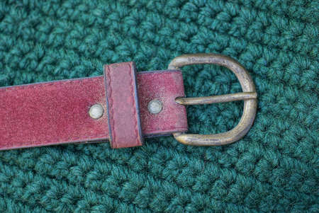 one red leather belt with a metal buckle rests on a green woolen fabricの写真素材