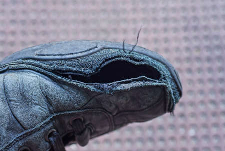 one old black torn leather boot with a big hole on a brown backgroundの写真素材