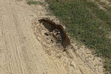 one pit pothole on the gray dry land of a rural road by green grass