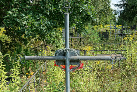 one gray iron cross on a grave in a cemetery overgrown with green vegetationの写真素材