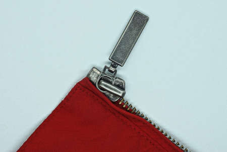 one gray metal open zip on a red cloth of clothing on a white tableの写真素材