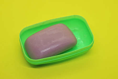 one purple bar of soap lies in an open green plastic soap dish on a yellow tableの写真素材
