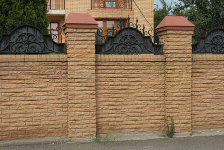 part of a brown wall of a brick fence on the street on gray asphaltの写真素材