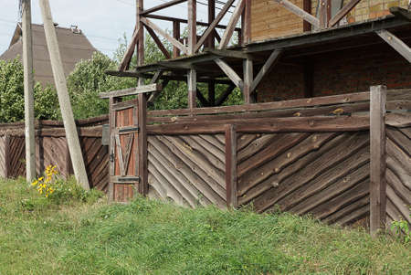 one closed old wooden door and part of a long brown fence wall on a rural streetの写真素材