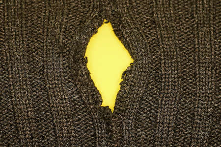 black background of fabric from torn clothes with a yellow holeの写真素材