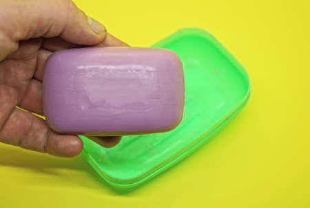 hand holds one purple soap over a green plastic soap dish on a yellow tableの写真素材