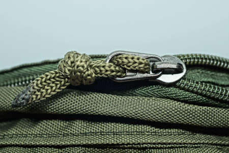 one gray metal zip with a drawstring on a green fabric of a backpack on a white background