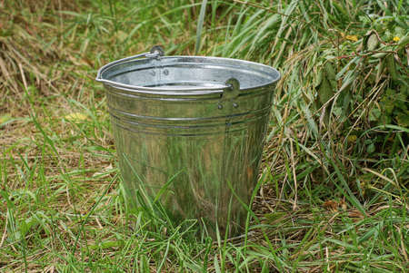 one gray large galvanized metal bucket stands outside in the green grassの写真素材