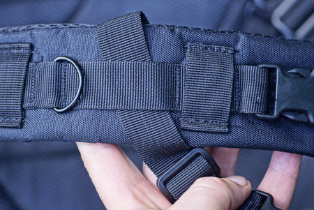 hand holds a one big black fabric harness with a metal ring on the tactical backpack