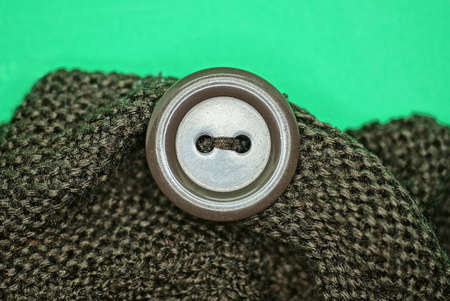 one big brown button on a piece of woolen clothes on the green background