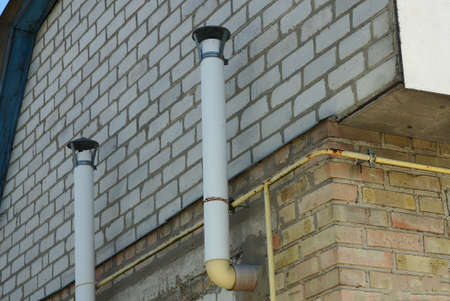 two white metal chimney pipes on a brick wall of a house on the street