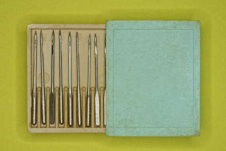a set of metal sewing needles in a brown plastic box with a gray lid lies on a yellow table