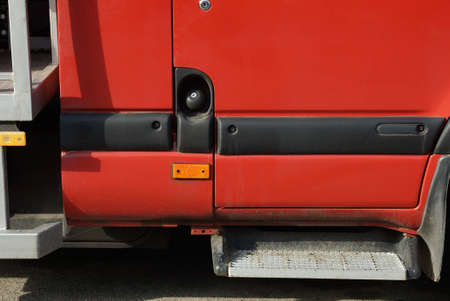 part of a red passenger car with a black closed gas tank cap on the street