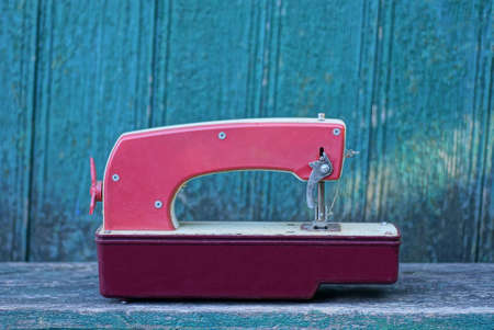 One old red toy car is standing on a gray table against a green wooden wall
