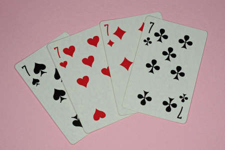 four playing cards of sevens lie on a pink table