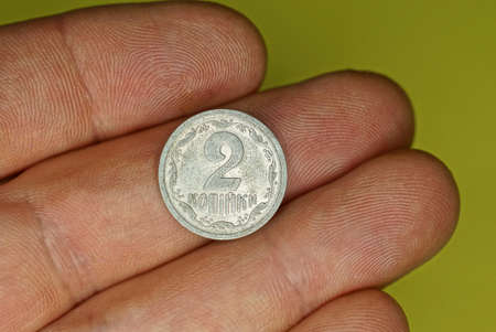 one white Ukrainian coin two kopecks lies on the fingers on a yellow background