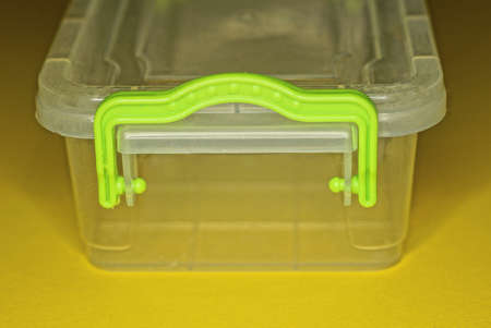 part of an empty white plastic food box with a green handle stands on a yellow table