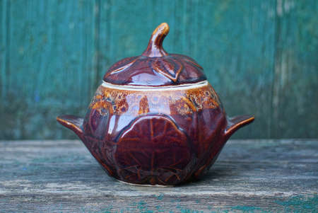 one closed brown ceramic pot stands on a gray wooden table against a green wall