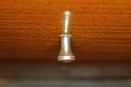 one small gray decorative doorknob on a brown wooden dresser boardの写真素材
