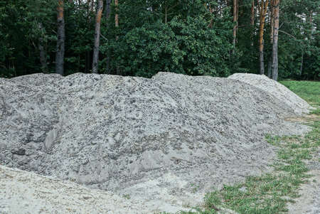 one big white pile of sand in the green grass on the street near a trees