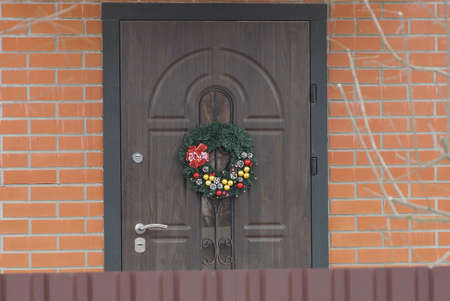 christmas wreath hanging on a brown door on a red brick wall at home on the streetの写真素材