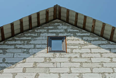 attic of a white brick private house with one small window against a blue sky