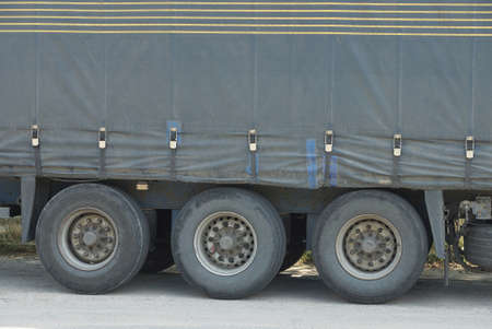 three black wheels on a gray large canvas truck trailer on the street on the asphalt road