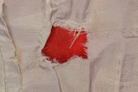 fabric texture from a piece of gray crumpled clothing with a red torn holeの写真素材