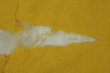 a large hole with white cotton wool on the yellow fabric of an old jacket