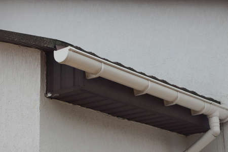 long white plastic gutter pipe on brown gray wall of a building on the street
