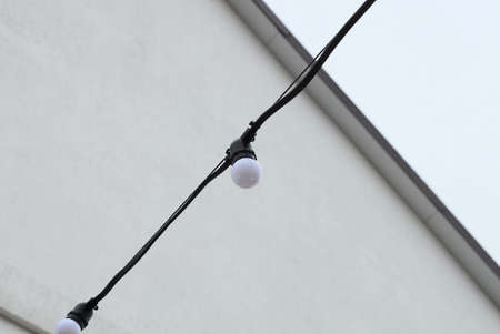 one small white light bulb on a black electric wire on the street against a gray wall