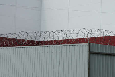 gray metal fence with barbed wire on the street against the background of a white red wall