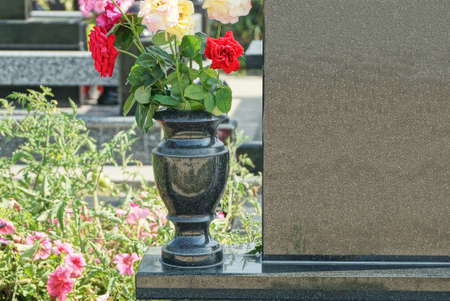 black marble vase with colored rose flowers at a gray granite monument on a grave in a cemetery