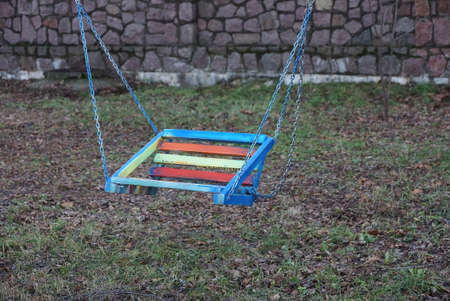 one colored child seat on a swing with metal chains in a park on the streetの写真素材