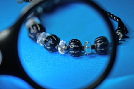 a round magnifying glass magnifies the jewelry bracelet with black and white beads on a blue tableの写真素材