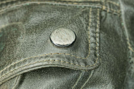 one old metallic gray rivet button on the black leather of an old dirty jacketの写真素材