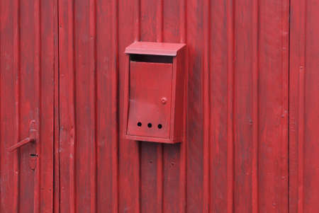 one black iron mail box hanging on a red metal fence wall in the street