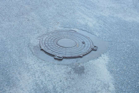 one brown wet iron sewer manhole on the gray asphalt on the streetの写真素材