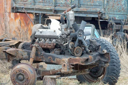 disassembled old rusty brown car with wheels and a motor in the grass on the streetの写真素材