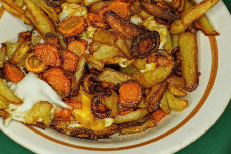 food of fried potatoes with carrots and scrambled eggs in a white plate on a green tableの写真素材