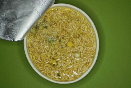 yellow soup with noodles in a white paper plate stands on a green table