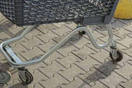 part of an empty gray black plastic metal trolley with a small wheel stands on the sidewalk on the...