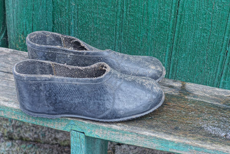 two old black dirty rubber galoshes stand on a gray wooden bench near a green wall on the street