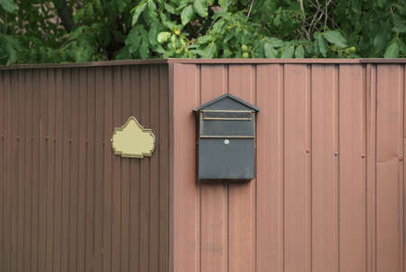one old black mailbox hanging on a brown metal fence wall in the streetの写真素材