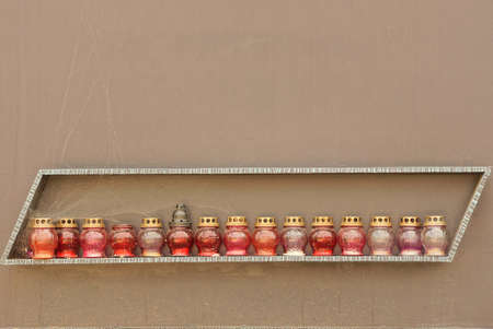 a row of red glass memorial lamps on a table against a brown concrete wall in a cemetery
