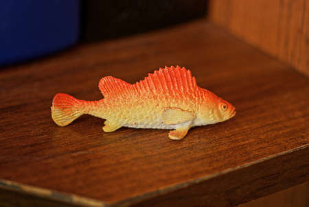 one small red yellow plastic toy fish lies on a brown table
